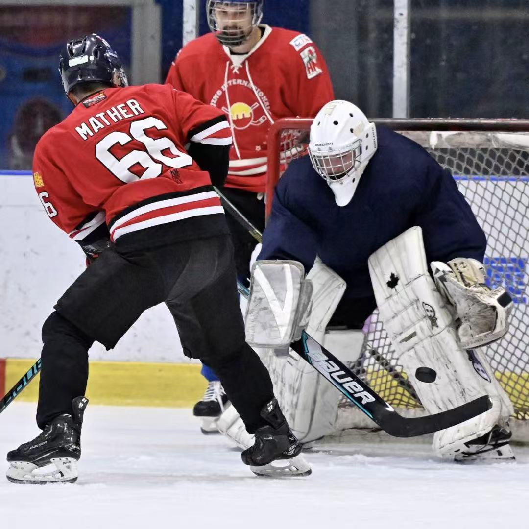 Goalie tracking the puck while a red-jersey player attacks the net